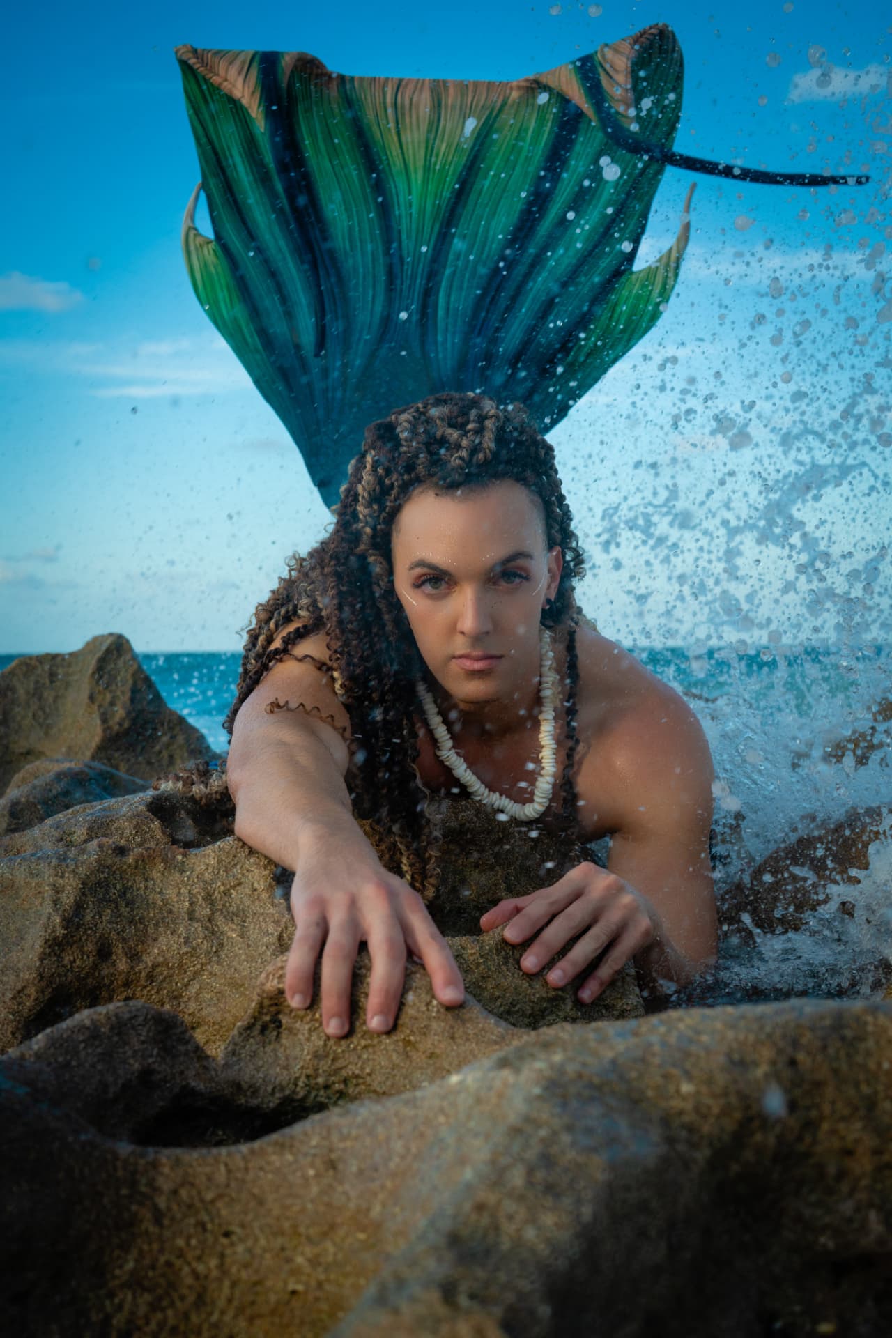 Prince Pōhaku resting on coastal rocks with a fan-shaped tail fin raised behind, waves breaking beside him